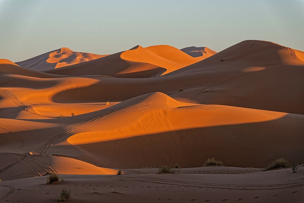 Women practicing meditation on Sahara desert dunes at sunset